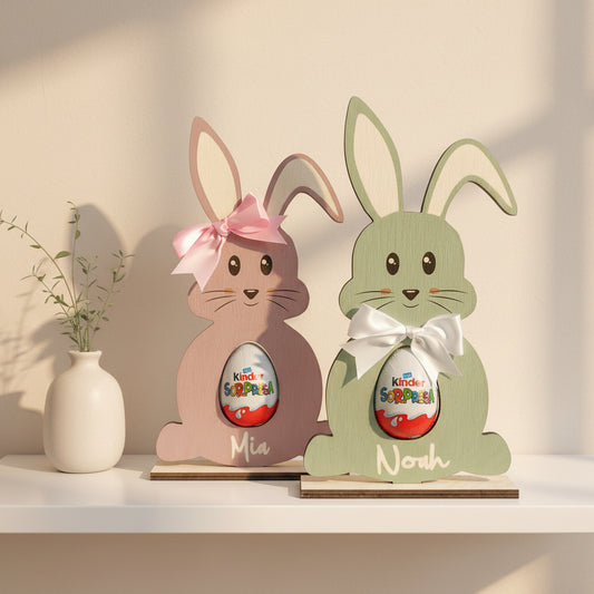 Two wooden bunny-shaped Easter decorations, one in pink and one in green, each with a personalized plaque that reads 'Kinder' and a name, MiA and NoH, respectively.